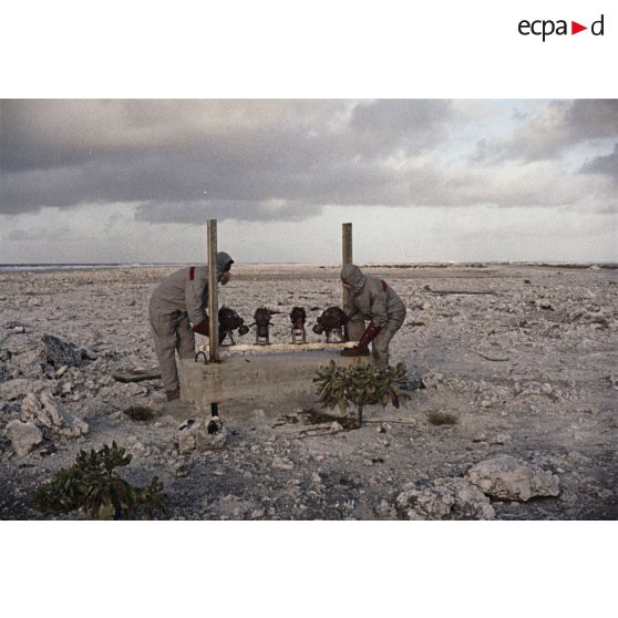 Près du poste d’enregistrement avancé (PEA) Denise, des personnels en tenue NBC relèvent des masques à gaz exposés pour étude des effets des tirs par la section technique de l’armée de terre (STAT).