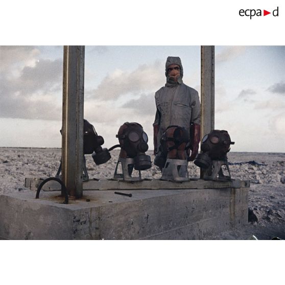 Près du poste d’enregistrement avancé (PEA) Denise, des personnels en tenue NBC relèvent des masques à gaz exposés pour étude des effets des tirs par la section technique de l’armée de terre (STAT).