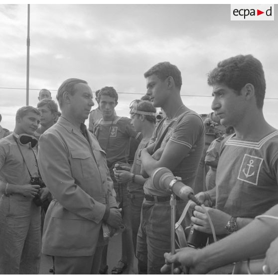 Michel Debré, ministre d'Etat chargé de la Défense, suite à l'expérience atomique du tir Licorne du 3 juillet 1970, s'entretient avec les jeunes marins du croiseur de commandement De Grasse équipés de lunettes de protection.