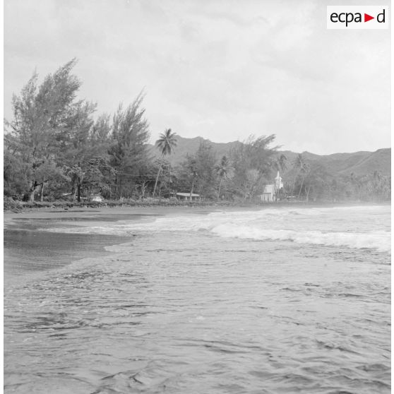 Paysage littoral de Polynésie française, probablement à Tahiti. En arrière-plan, une église.