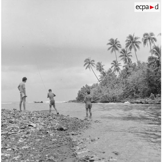 Paysage de Polynésie française, probablement à Tahiti. Des enfants pêchent à l'embouchure d'une rivière.