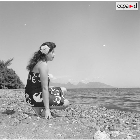 Fêtes du Juillet ou fête du Tiurai à Papeete en 1964. Portrait d'une jeune femme polynésienne au bord du rivage. En arrière-plan, l'île de Moorea.