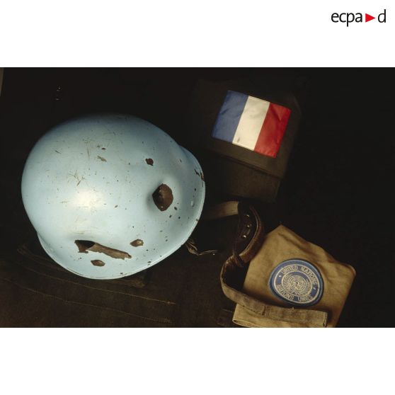 Vue d'au-dessus d'un casque bleu d'un sergent du 8e régiment d'infanterie (8e RI) ayant été blessé à la tête par balle en ex-Yougoslavie mis en scène sur une veste militaire avec le drapeau français et l'insigne de l'ONU.