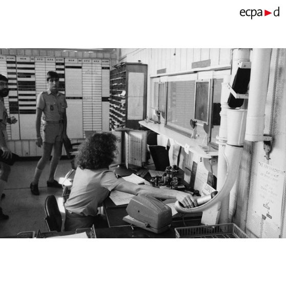 Le groupement de transmission terre (GTT) 815 à l'état-major du Taaone : commandement, exploitation, centre de relais bande. Un caporal féminin place une capsule dans le réseau de transport par tube pneumatique (air comprimé).