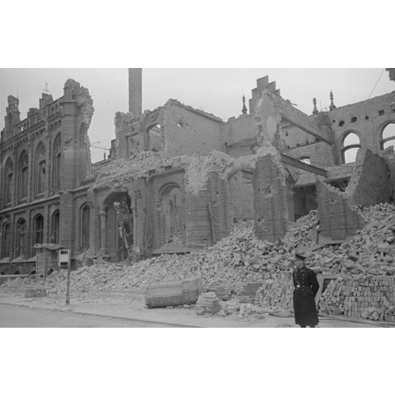 Des bâtiments en ruine avec un homme en uniforme se tenant devant, sur la route.