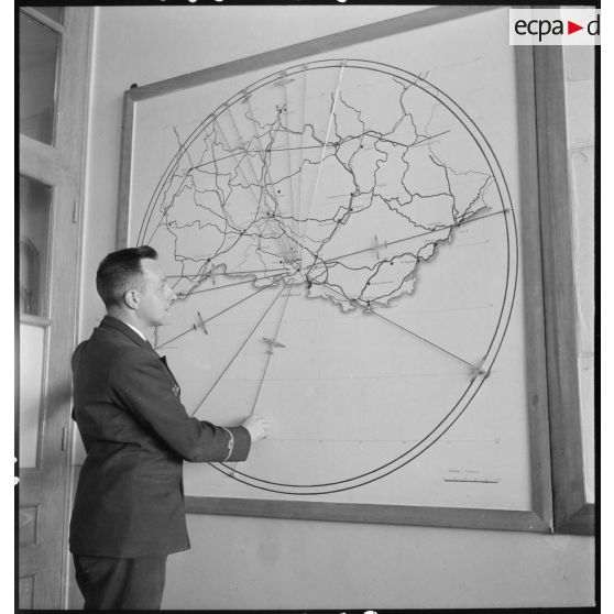 Personnel d'Air France, a priori un chef de cabine, devant une carte figurant les liaisons aériennes de la compagnie.