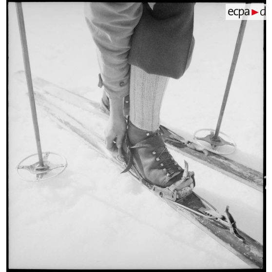 Un participant chausse ses skis avant un concours de ski de l'organisation Jeunesse et Montagne dans les Alpes.