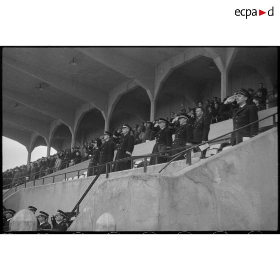 Lors d'une fête sportive au stade de Vichy sous la présidence d'un général de brigade aérienne, les autorités présentes dans les tribunes saluent le drapeau lors de la montée des couleurs.