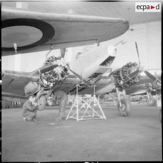 Des mécaniciens travaillent sur le train d'atterrissage d'un avion de chasse Potez 630 ou 631 dans un hangar de la base aérienne d'Ambérieu-en-Bugey.