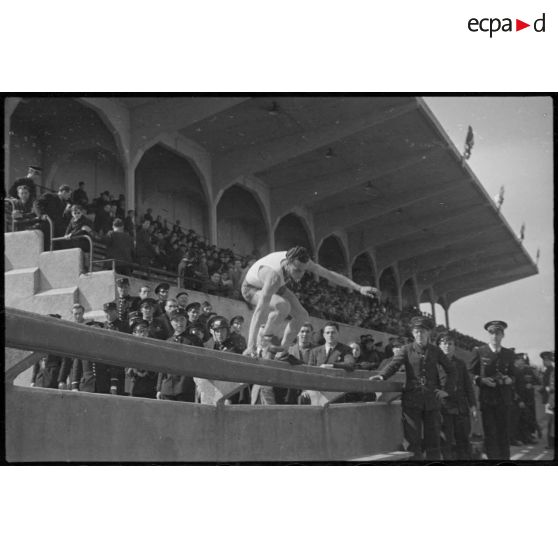 Un athlète franchit une barrière sur le stade de Vichy lors d'une manifestation sportive de l'armée de l'Air rassemblant plusieurs unités.