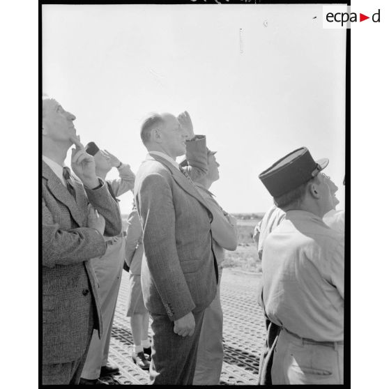 M. Grenier ainsi que le général Bouscat et les gagnants du tirage de la tombola admirent les acrobaties d'un chasseur sur le terrain de Réghaia.
