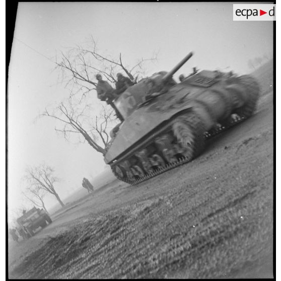 Un char Sherman du 4e escadron du 2e RC (Régiment de cuirassiers) progresse sur une route au nord-est de Mulhouse (Haut-Rhin), suivi par un half-track, pour mener une contre-attaque. [description provisoire]