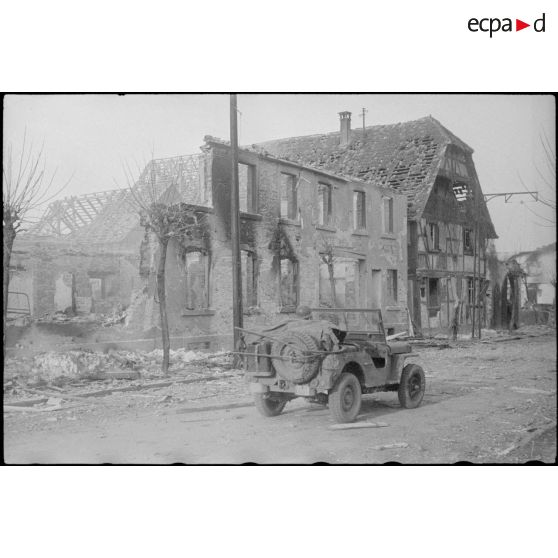 Une jeep traverse Rhinau (Bas-Rhin) en ruine ; la ville a été bombardée par des tirs de mortier allemand le 27 décembre 1944. [description provisoire]