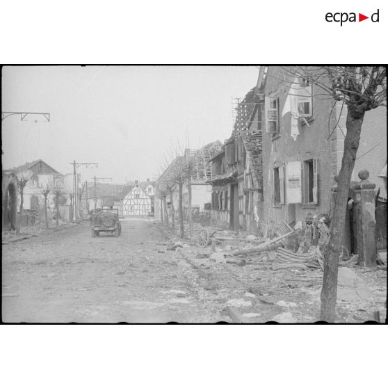 Une jeep traverse Rhinau (Bas-Rhin) en ruine ; la ville a été bombardée par des tirs de mortier allemand le 27 décembre 1944. [description provisoire]