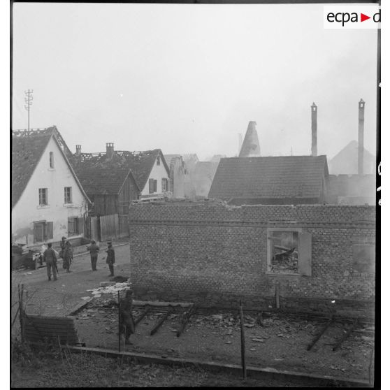 Rhinau (Bas-Rhin) est en proie aux flammes et en ruine, le village alsacien ayant été bombardé par les Allemands entre le 10 et le 22 décembre 1944. Les troupes avancent dans la commune dévastée. [description provisoire]