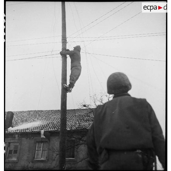 Pose de lignes téléphoniques dans un village du front dans la région de Sarreguemines (Moselle) par le génie américain. [description provisoire]