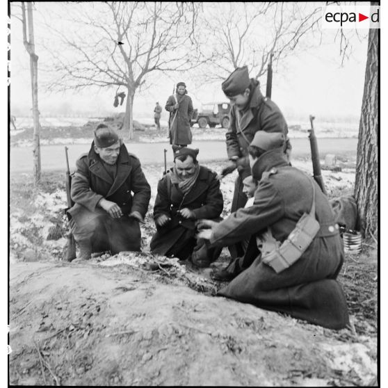 Des canonniers d'une section du 21e groupe antillais des FTA (Forces terrestres antiaériennes), qui fait partie de la 1re DMI (Division de marche d'infanterie) (ex 1re DFL), se réchauffent autour d'un feu près d'Obernai (Bas-Rhin) dont ils doivent assurer la défense. [description provisoire]