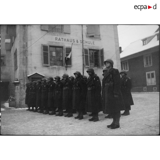 Détachement de la 9e DIC (Division d'infanterie coloniale) en rang devant la mairie et l'école du village de Steinbrunn-le-Bas (Haut-Rhin) à l'occasion de la visite d'attachés militaires étrangers sur le front d'Alsace. [description provisoire]