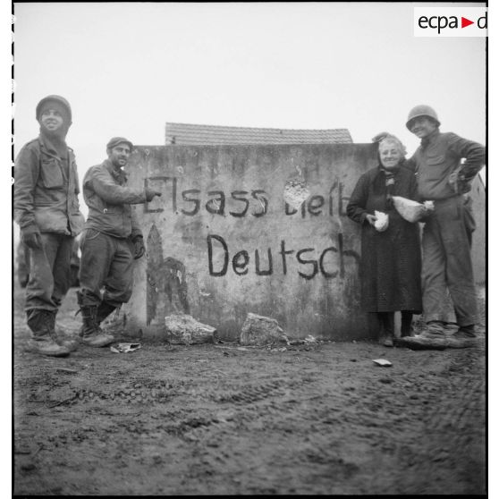 Une habitante du village de Wolfgantzen (Haut-Rhin) à peine sortie de sa cave où elle s'était réfugiée pendant l'attaque du village, donne du pain aux soldats. [description provisoire]