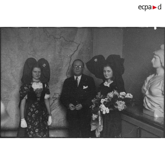 Portrait du ministre à la Guerre, André Diethelm, et de deux jeunes femmes revêtues du costume traditionnel alsacien, à Paris. [description provisoire]