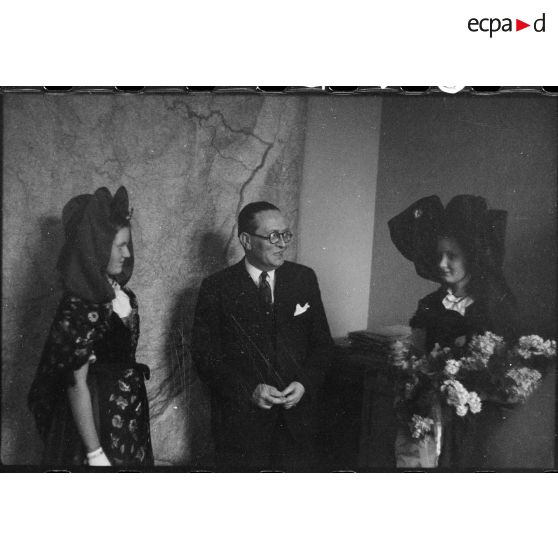 Le ministre à la Guerre, André Diethelm, reçoit deux jeunes femmes revêtues du costume traditionnel alsacien, à Paris. [description provisoire]