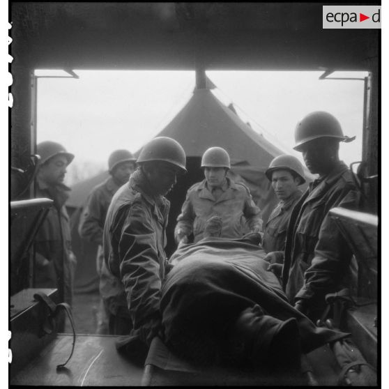 Evacuation depuis un poste sanitaire d'un blessé par des brancardiers nord-africains du 13e bataillon médical (BM 13) de la 2e division blindée (2e DB). [description provisoire]