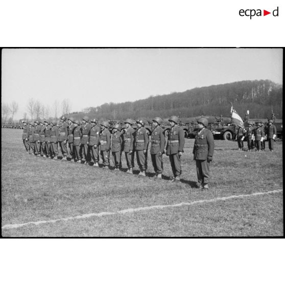 Alignement d'hommes du 1er bataillon de zouaves tout juste décorés par le général Sudre, commandant la 1re DB (Division blindée), lors d'une prise d'arme à Hindlingen (Haut-Rhin) le 19 mars 1945. [description provisoire]