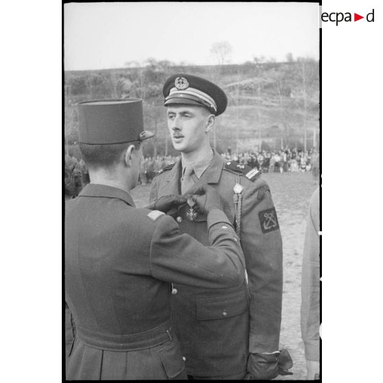 Au cours d’une prise d’armes, le général de division Philippe Leclerc remet la croix de guerre à l’enseigne de vaisseau Philippe de Gaulle, commandant un peloton de combat du Régiment blindé de fusiliers marins (RBFM). [description provisoire]