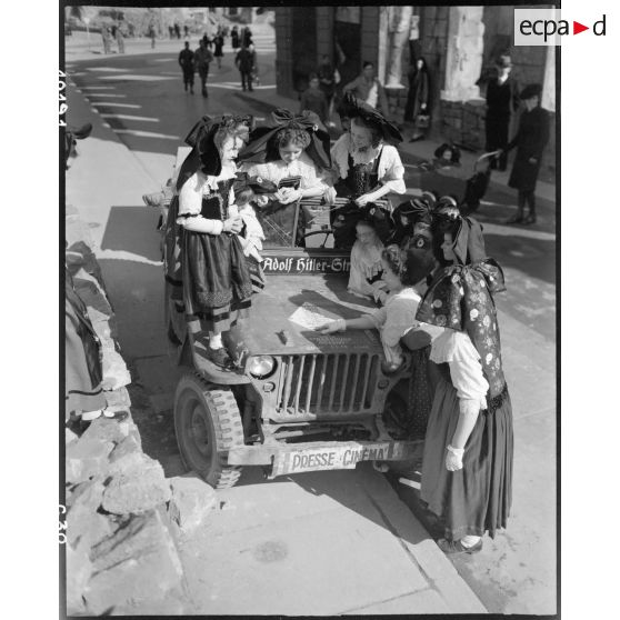 A Strasbourg, des Alsaciennes en costume entourent la jeep "Presse Cinéma" du SCA. [description provisoire]