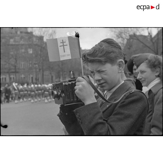 Jeune homme photographiant le défilé des troupes à l'arc de triomphe de l'Etoile à Paris lors d'une cérémonie le 2 avril 1945. [description provisoire]