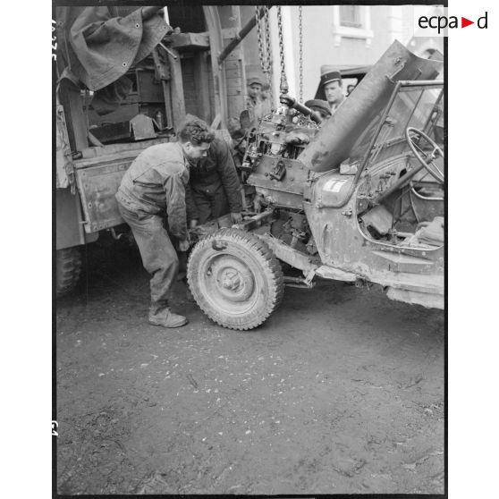 Mise en place ou dépose d'un moteur de jeep à l'aide d'un palan par des mécaniciens de la section matériel de la compagnie mixte de transmissions 97/84 de la 2e division blindée (2e DB).