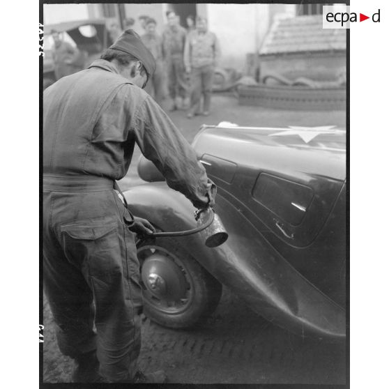 Peinture au pistolet de marquages sur une Citroën traction avant dans l'atelier de réparation automobile de la compagnie mixte de transmissions 97/84 de la 2e division blindée (2e DB).