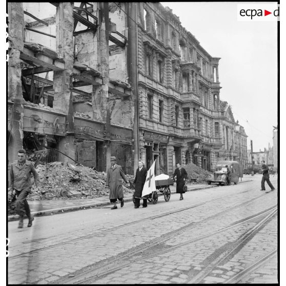 La Croix-Rouge dans une rue de Karlsruhe en ruine. A l'arrière-plan, un véhicule du service cinématographique de l'armée (SCA).