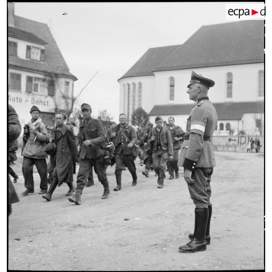 Dans un village du Bade-Würtemberg, un feldgendarme regarde passer des prisonniers allemands. [description provisoire]