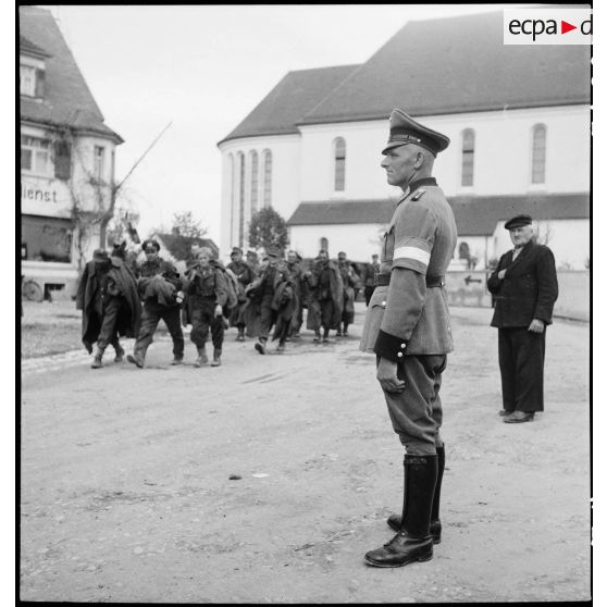 Dans un village du Bade-Würtemberg, un feldgendarme regarde passer des prisonniers allemands. [description provisoire]