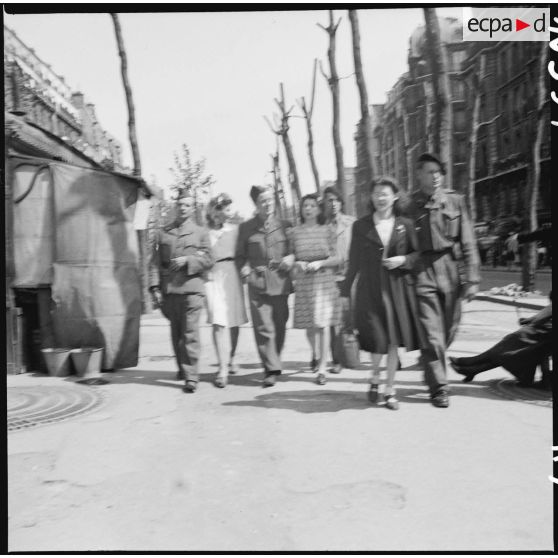Des soldats français déambulent avec des parisiennes sur un grand boulevard de Paris.
