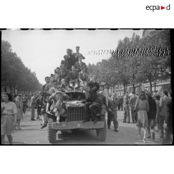 Population civile et militaires français et américains embarqués sur des véhicules circulant sur les Champs-Elysées.