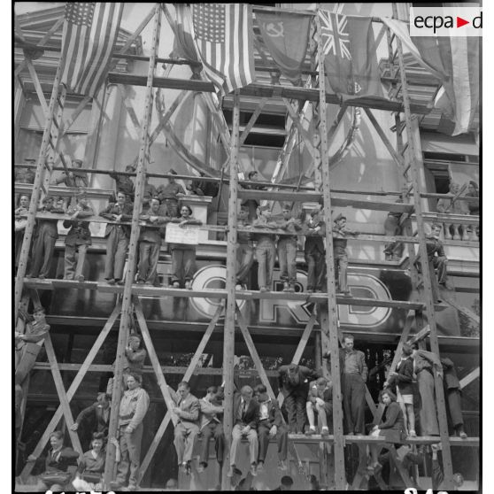 Civils et militaires sont juchés sur des échafaudages sur les Champs-Elysées, à l'occasion de la visite du général Eisenhower à Paris.
