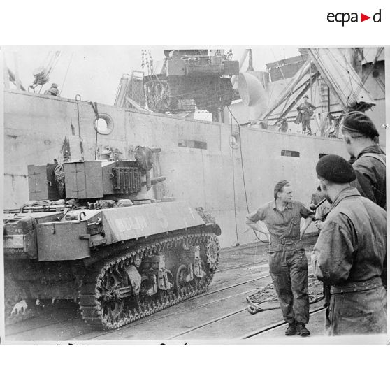 Embarquement de matériels et de véhicules de la 2e division blindée (2e DB)) dans des bâtiments de débarquement LST depuis un quai en Angleterre à destination de la Normandie.