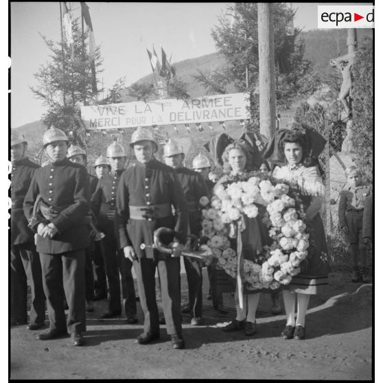 Photographie de groupe : soldats accompagné de deux jeunes Alsaciennes portant une gerbe de fleurs.