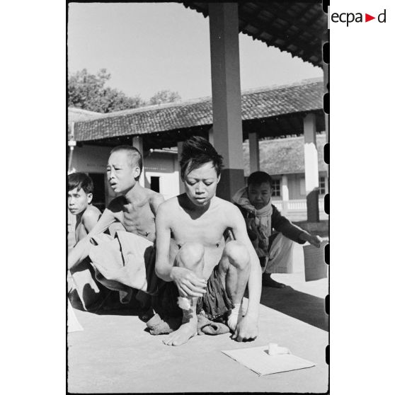 Gros plan de deux coolies dont l' un avec un pansement et un bandage aux jambes. Ces deux coolies sont amaigris et malades du fait d' être restés plusieurs mois dans les rangs de viêt-minh mal logés et mal nourris.