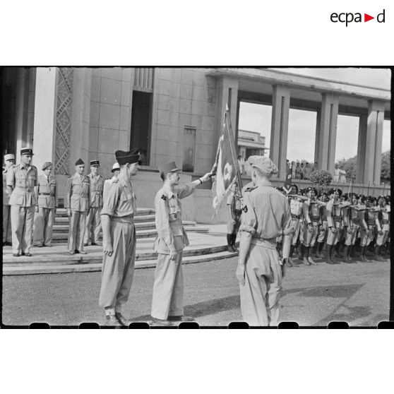 Le général LECLERC tenant le drapeau du régiment des tirailleurs cambodgiens et lisant les noms des combats qui y sont inscrits.