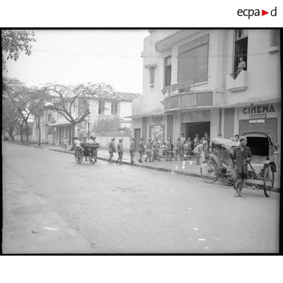 Militaires chinois en attente devant un cinéma. Au premier plan, un enfant tirant un pousse-pousse.