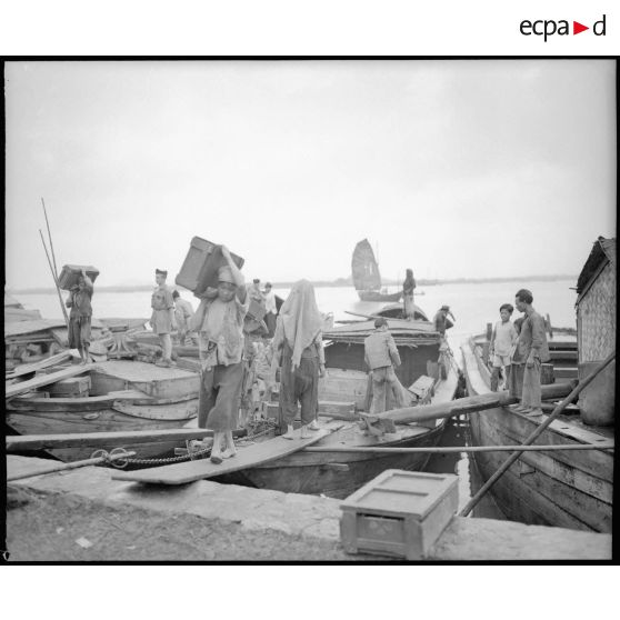 Déchargement de caisses de bois de barques par des tonkinois (hommes, femmes, et enfants.