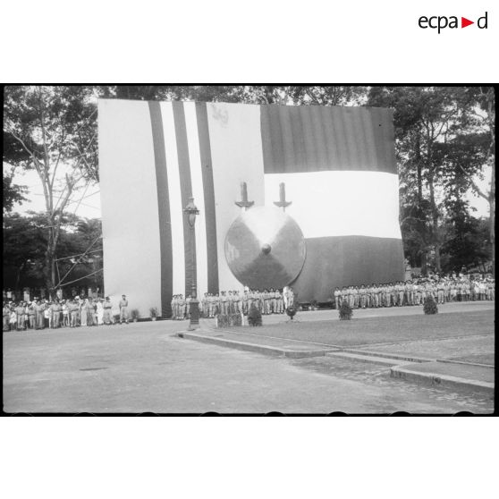 Pendant la cérémonie : troupes de soldats devant un énorme drapeau fait du drapeau vietnamien et du drapeau français.