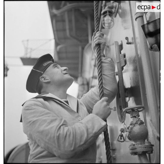 Portrait de Jean Kerlevéo, prêtre marin, affecté à bord du croiseur Georges Leygues, tirant probablement sur la corde de la cloche du navire.