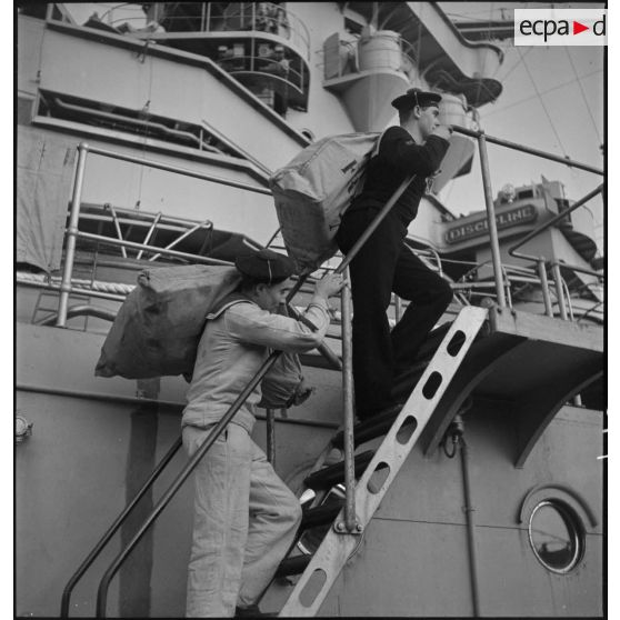 Un vaguemestre monte des sacs postaux à bord du cuirassé Strasbourg au mouillage dans la rade de Brest.