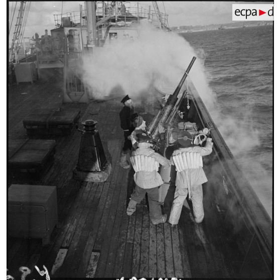 Des canonniers ouvrent le feu sur un objectif avec un canon antiaérien de 37 mm à bord d'un cargo naviguant en convoi, réquisitionné et armé par la Marine nationale (reproduction).