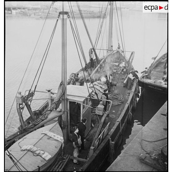 Un chalutier réquisitionné et armé par la Marine nationale est à la manoeuvre pour accoster dans un port.