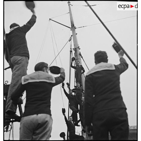 Des marins français saluent des marins britanniques montés dans la mâture d'un navire.
